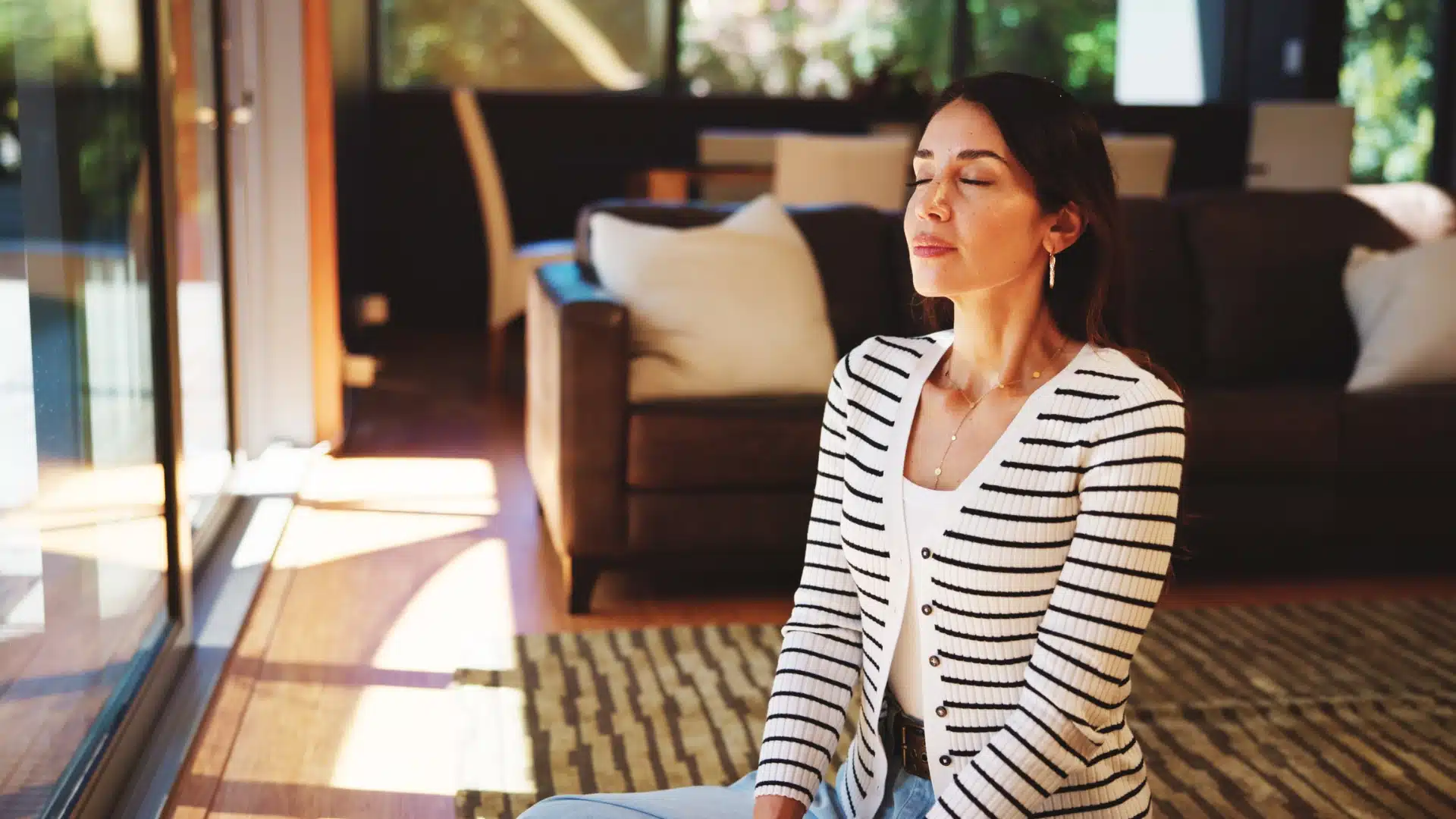 Woman relaxing at home with eyes closed, focusing on slow, deep breathing