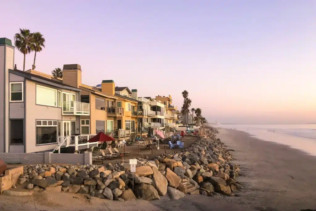 Oceanside beachfront homes along a rocky shoreline overlooking the Pacific Ocean at sunset