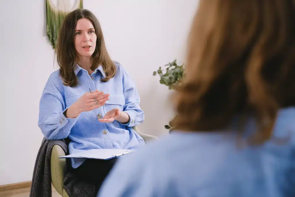 A woman seated in a chair engages in conversation with another woman nearby.