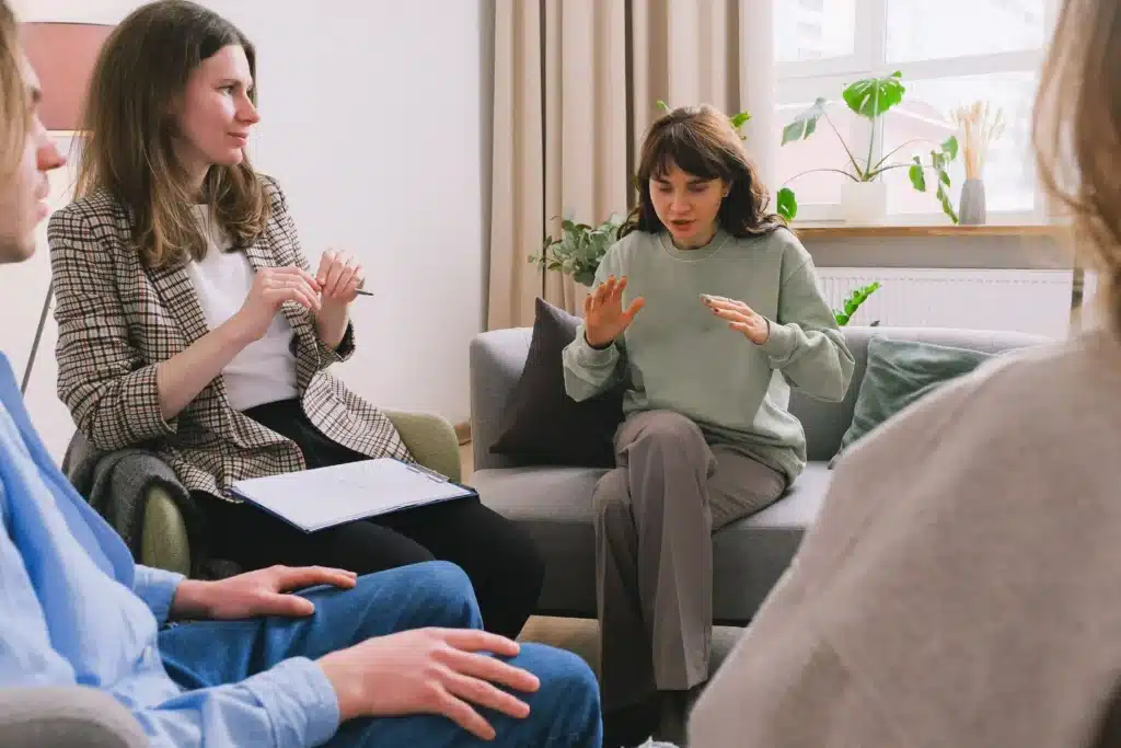 A group of four people engaged in conversation while sitting on a comfortable couch in a cozy living room setting.