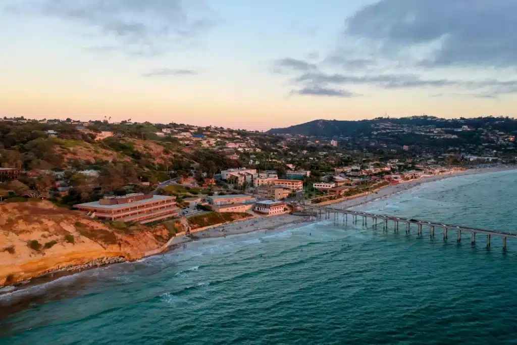 Aerial view of San Diego's ocean and beach at sunset, showcasing vibrant colors reflecting on the water.